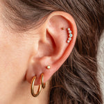Close-up of a person's ear showcasing multiple gold and pearl ear piercings, including hoop earrings, a stud, and a curved row of small white pearls on the helix.