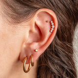 Close-up of a person's ear showcasing multiple gold and pearl ear piercings, including hoop earrings, a stud, and a curved row of small white pearls on the helix.