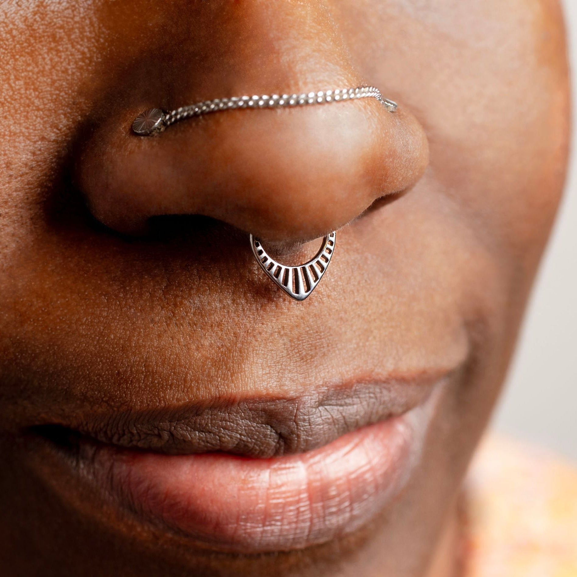 Close-up of a person wearing a silver nose ring with a chain on a neutral background