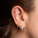 Close-up of a person's ear showcasing multiple pieces of gold and silver-toned piercing jewelry, including a curved cartilage bar, small studs, and hoop earrings.