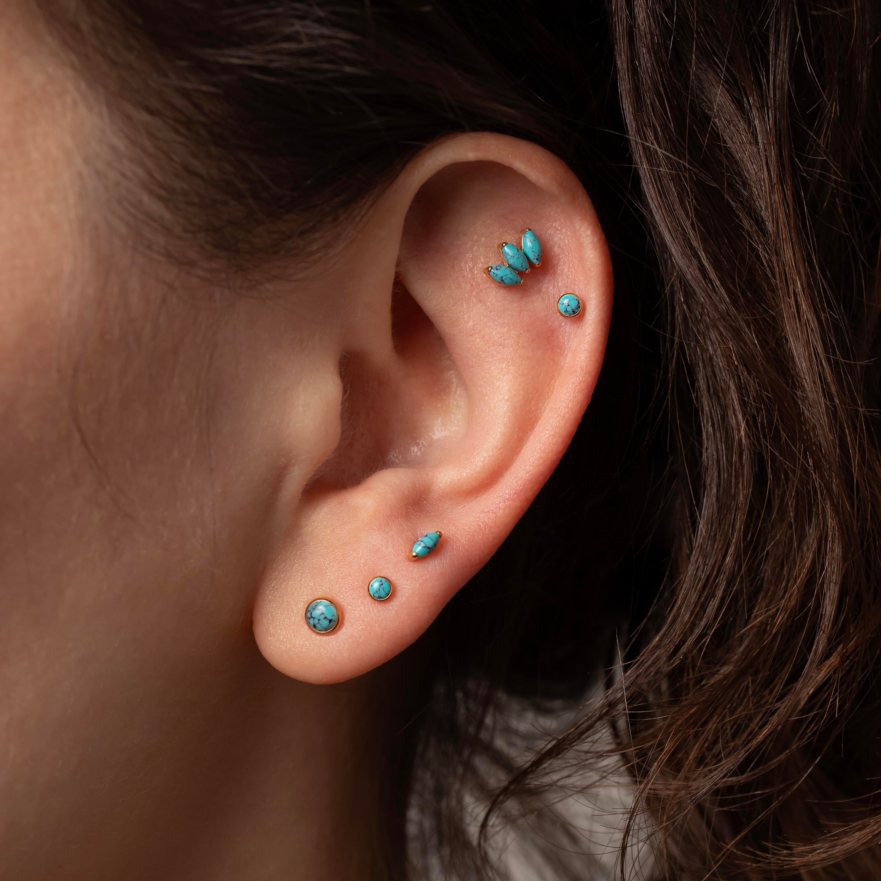 Close-up of an ear with turquoise earrings against a dark background