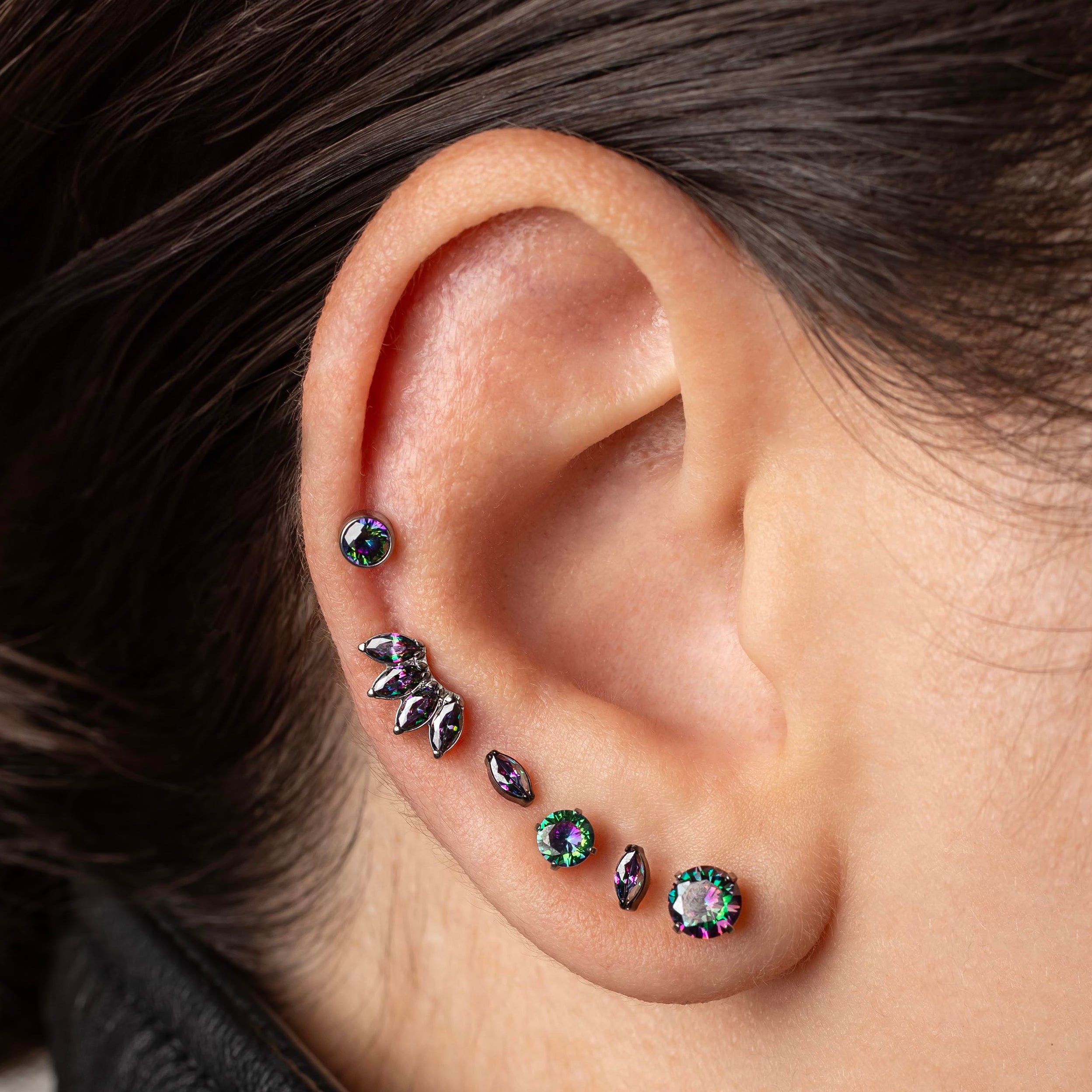 Close-up of an ear with multiple earrings on a neutral background