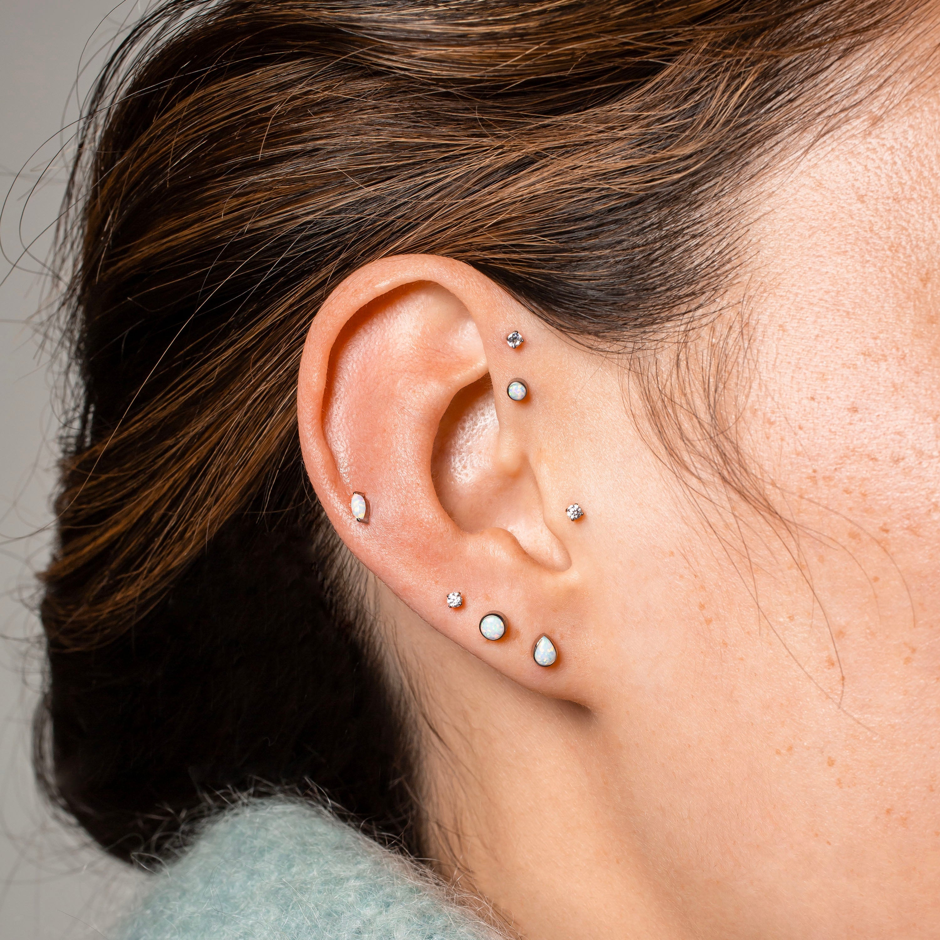 Close-up of an ear with multiple earrings against a neutral background