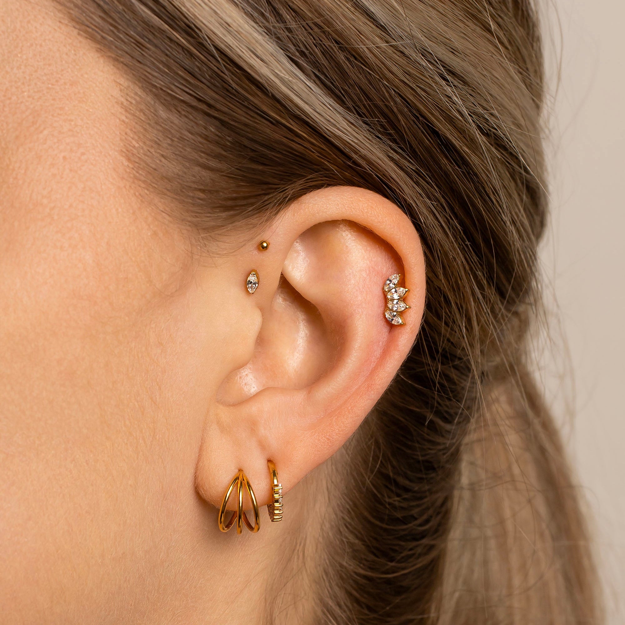Close-up of an ear with gold and silver earrings against a neutral background