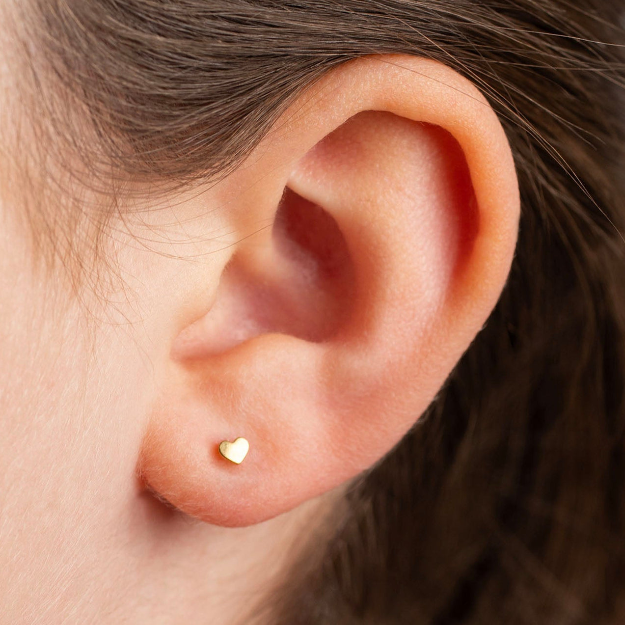 Close-up of an ear wearing a gold earring with hair partially covering the face.