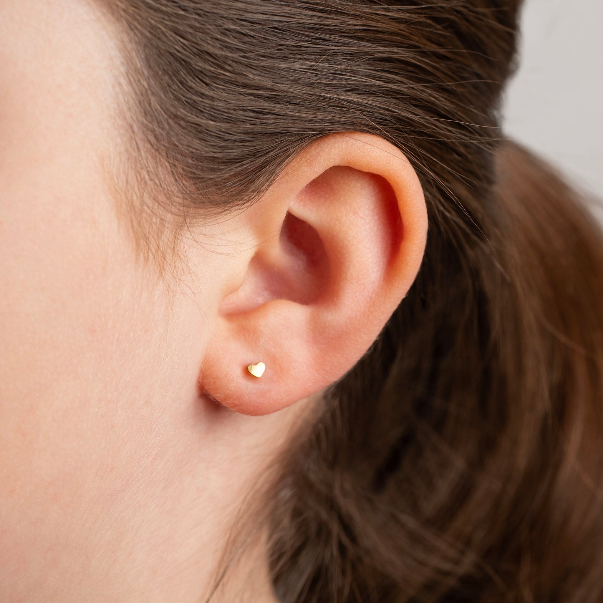Close-up of an ear wearing a gold earring with hair partially covering the face.