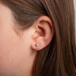 Close-up of an ear wearing a diamond stud earring with hair partially covering the frame.