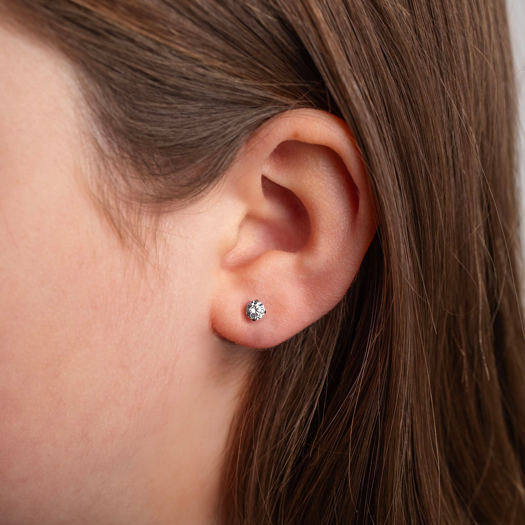 Close-up of an ear wearing a diamond stud earring with hair partially covering the frame.