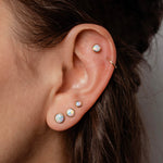 Close-up of an ear with multiple pearl earrings on a neutral background