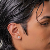 Person with styled hair wearing a white shirt against a neutral background with a conch piercing