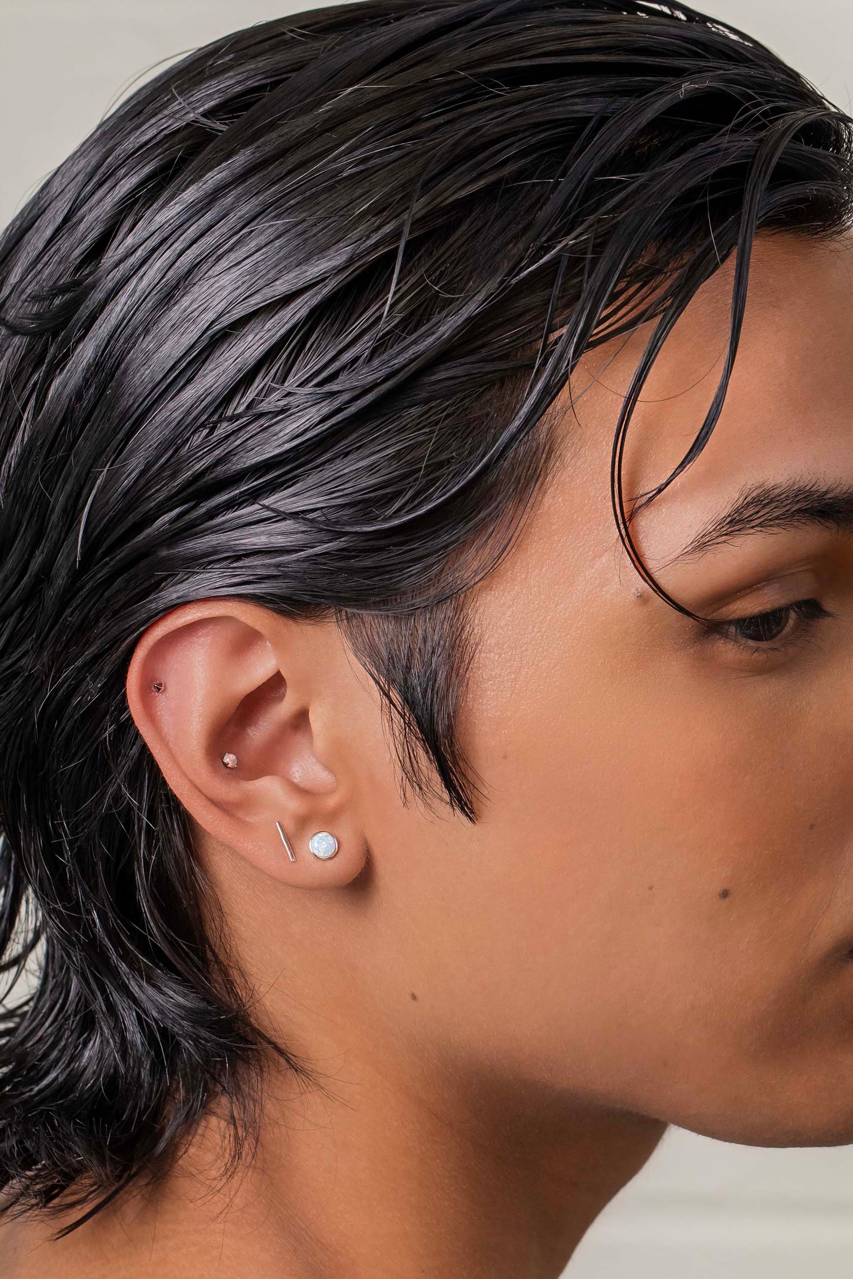 Person with styled hair wearing a white shirt against a neutral background with a conch piercing