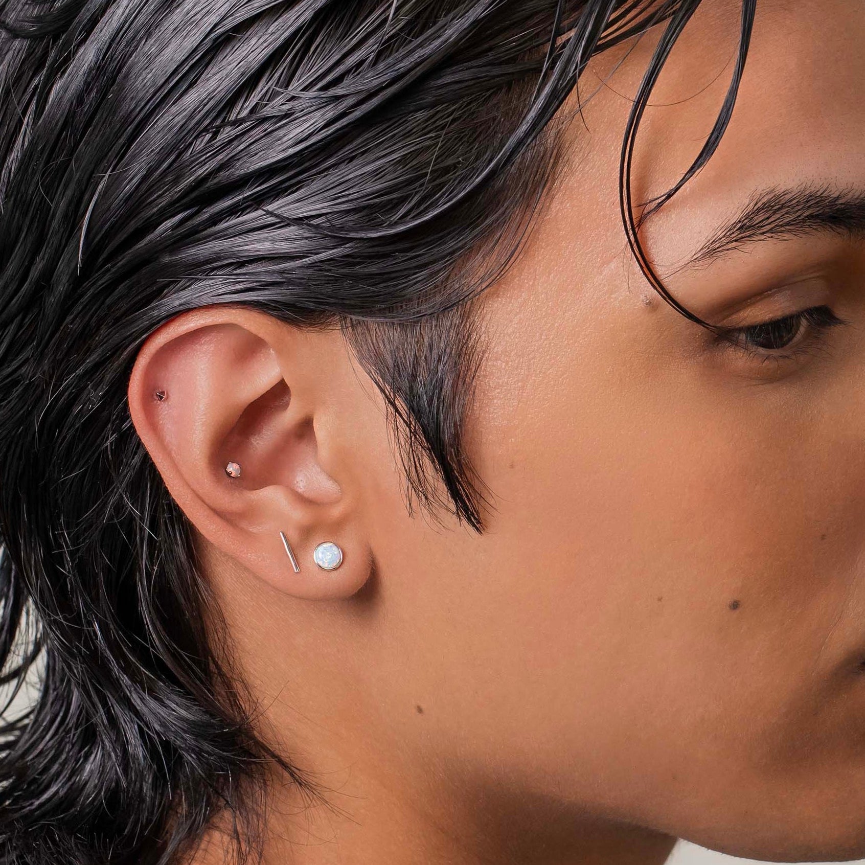 Person with styled hair wearing a white shirt against a neutral background with a conch piercing