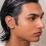 Man with styled hair wearing a light-colored sweater against a neutral background conch piercing