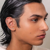 Man with styled hair wearing a light-colored sweater against a neutral background conch piercing