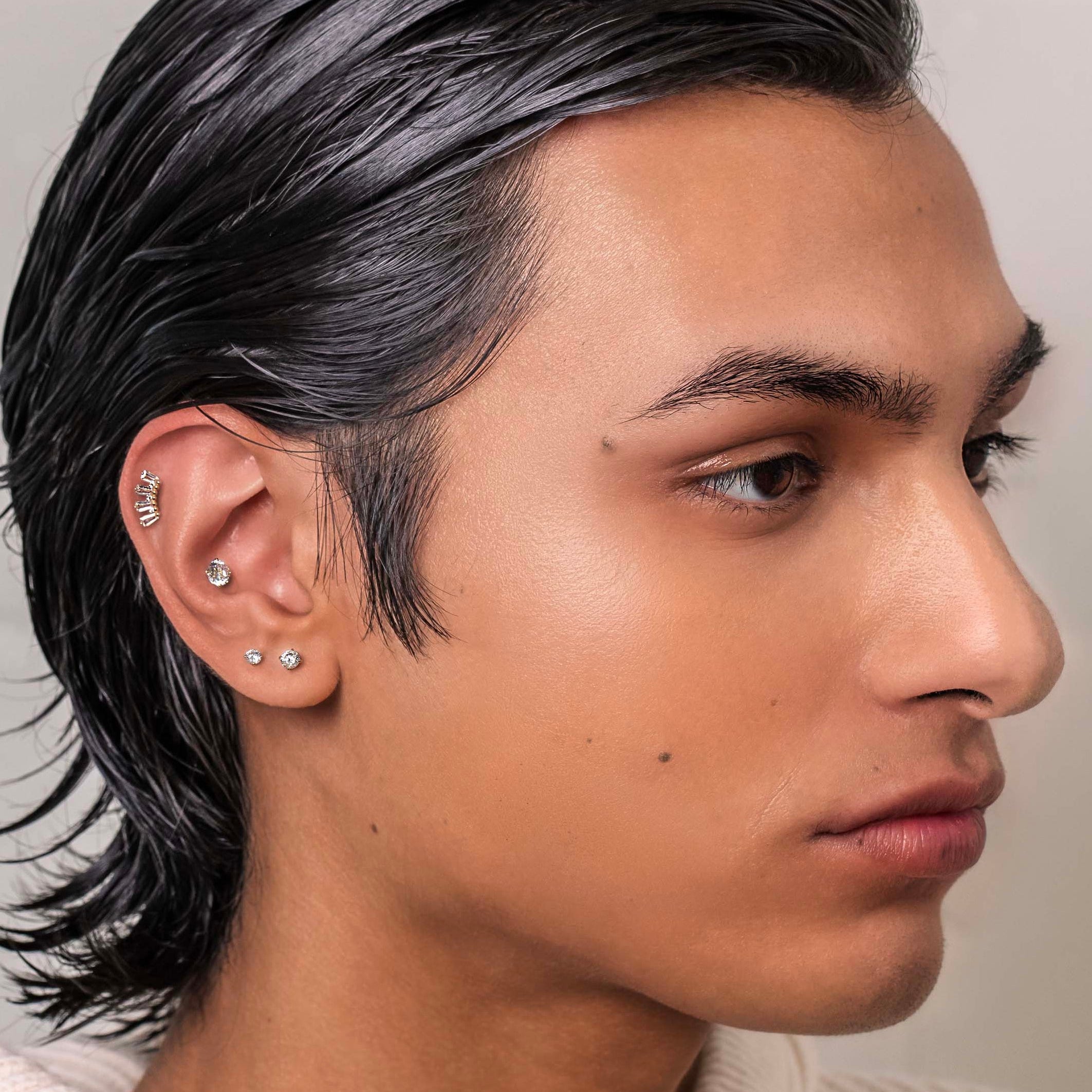 Man with styled hair wearing a light-colored sweater against a neutral background conch piercing
