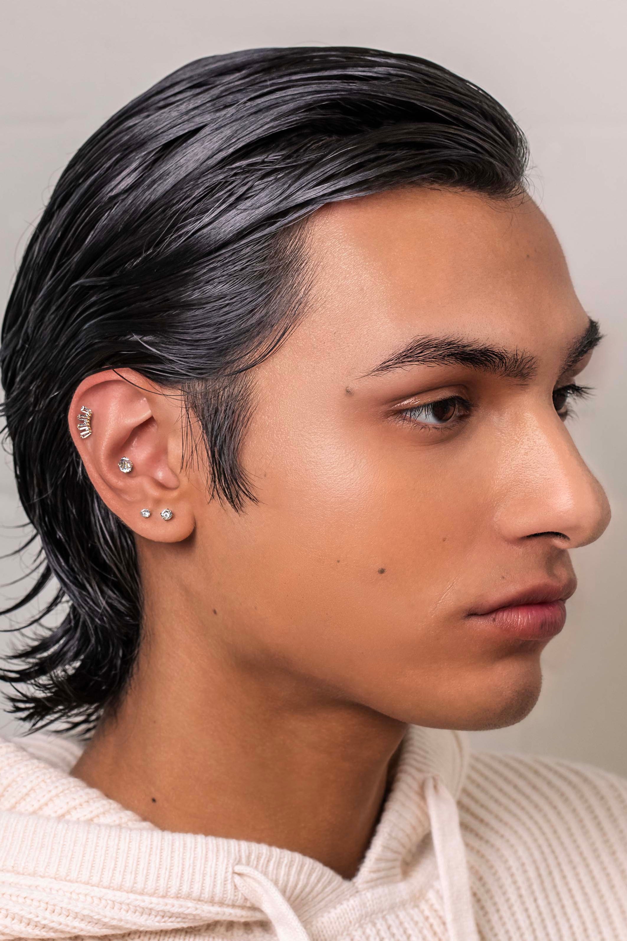 Man with styled hair wearing a light-colored sweater against a neutral background conch piercing