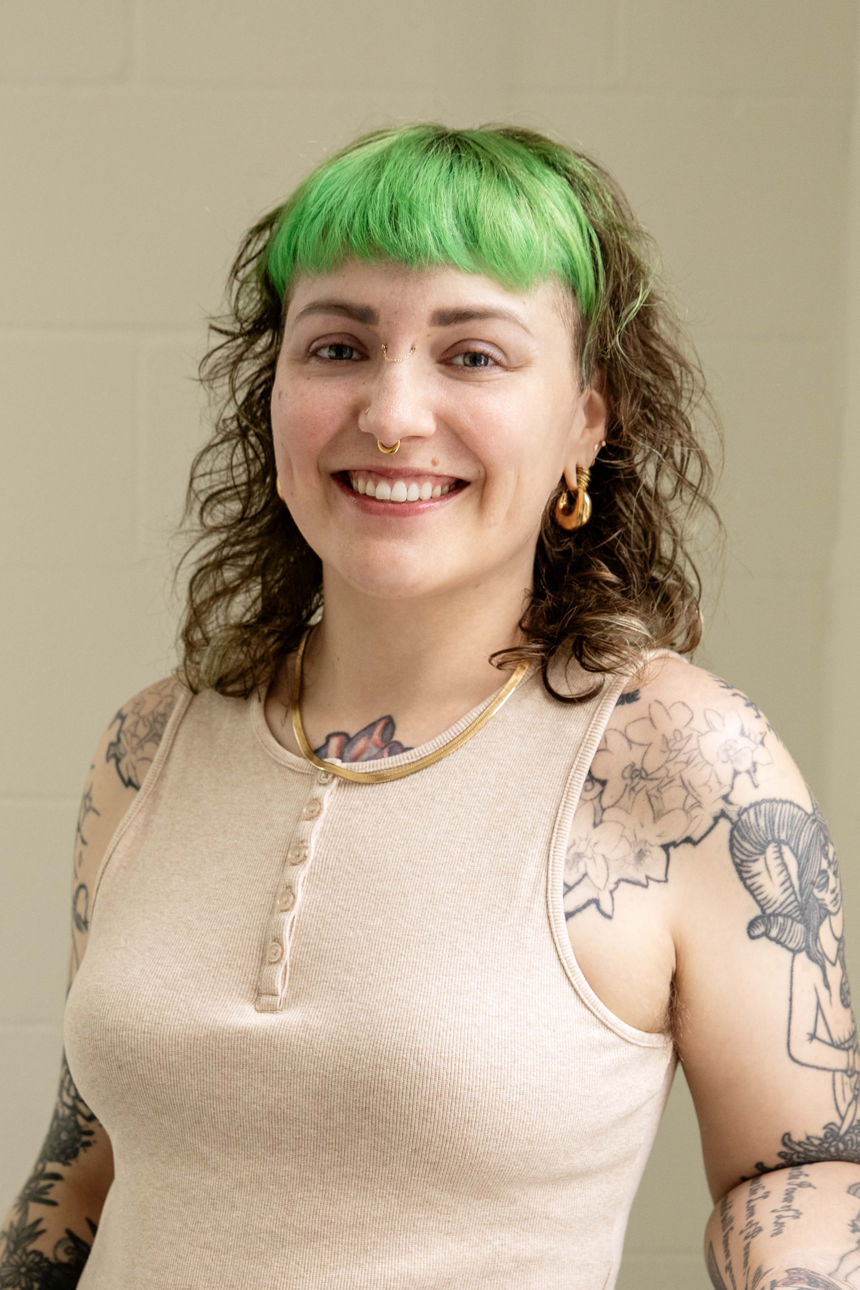 Person with green hair and tattoos on a plain background