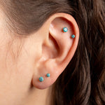 Close-up of a person's ear wearing four small turquoise-blue stud earrings on different cartilage locations.